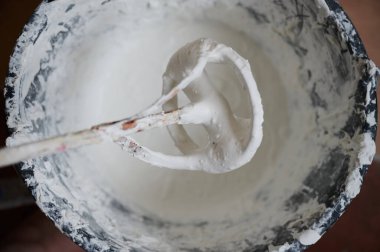 Mixer for building mixes in white liquid putty on the background of ready-made material for application to walls.