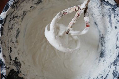 Mixer for building mixes in white liquid putty on the background of ready-made material for application to walls.