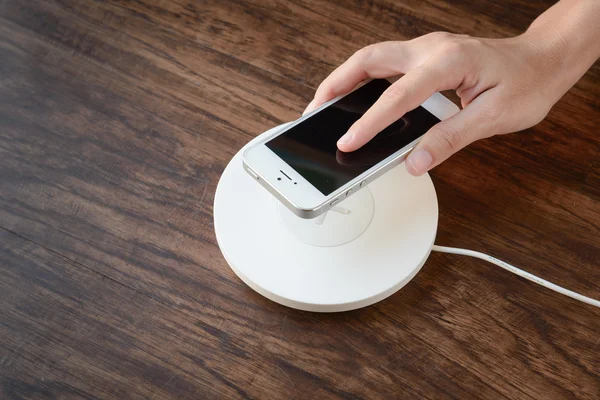 Una mano que pone el teléfono móvil en un cargador inalámbrico, equipo moderno — Foto de Stock