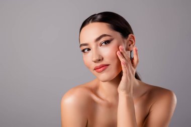 Makyajlı, parlak, pürüzsüz bir cilde sahip, parlak bir saç stiline sahip, tarafsız gri bir arkaplana karşı güzel ve zarif genç bir kadının yakın çekimi..