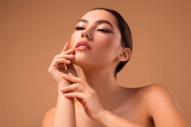 Bej bir arka plana karşı şık bir görünüm sergileyen genç bir kadın, pürüzsüz bir ten ve modern makyaj eğilimlerini vurgulayarak, güzellik, moda ve çağdaş bir estetik.