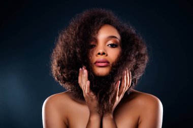 Kusursuz moda ve tarz sergileyen, güzelliği, kozmetiği ve kendine güveni vurgulayan çekici bir kadının zarif görüntüsü. Doğal kıvırcık saçlar ve parlak koyu bir arka plana karşı büyüleyici bir ifade..