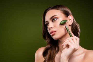 Yüz masajı için yeşim taşlı çekici esmer kadın. Cilt bakımı, gençleşme ve zarafet konsepti sergiliyor..