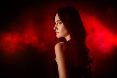 Dramatik kırmızı ve siyah bir arkaplanda poz veren genç ve güzel bir kadın, şehvet ve zarafeti resmediyor..