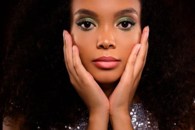 Doğal güzelliğini ve kalın makyajını sergileyen şık bir kadının yakın plan görüntüsü, zıt bir arkaplanda, samimi bir ifadeyle ve şık bir kıyafetle tasvir edilmiş..