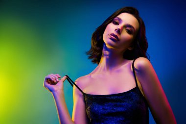 Dramatik neon ışıklarla poz veren büyüleyici bir genç kadın görüntüsü çarpıcı güzelliğini, modaya uygun görünümünü ve gece kulübü temalarının büyüleyici cazibesini vurguluyor..