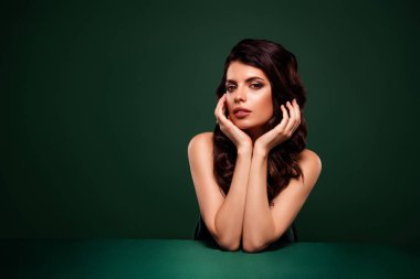 Kıvırcık esmer saçlı, kusursuz makyajlı ve çekici bir stili olan şık, genç bir kadının zarif portresi canlı yeşil bir arka planda yer alıyor..