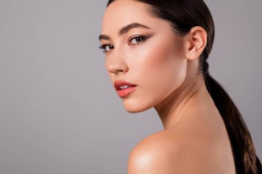 Parlak tenli, minimalist makyajlı ve gri arka planda şık saçlı genç bir kadın modelin stüdyo portresi..