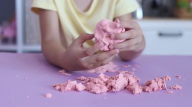 Çocuk elinde karıştırarak kinetik kumla oynuyor. Pembe kinetik anti-stres kumu olan çocukların ellerine yakından bakın. Çocuklar ve yetişkinler için stres önleyici oyuncak. 4k görüntü.