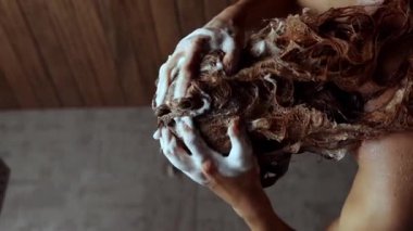 Avrupalı görünümlü genç bir kadın saçını duşta şampuanla yavaş çekimde yıkıyor. Günlük kişisel bakım kavramı. Saç bakım konsepti. Güzellik rutini. Yakın plan. Dikey görüntüler