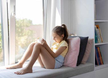 Tablet kullanan Avrupalı görünümlü küçük bir kız. Çocuk sanal oyunlar oynuyor ya da tabletinde çizgi film izliyor. Tabletli çocuk. Alet bağımlılığı sorunu..