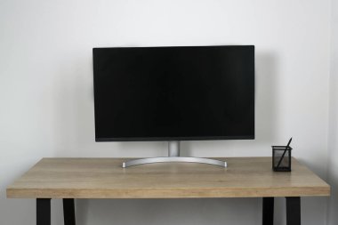 Ahşap bir masada beyaz bir duvara karşı modern siyah bir bilgisayar monitörü olan minimalist çalışma alanı. Ofisin içini kopyalama alanı ve basit, çağdaş tasarım ile temizle