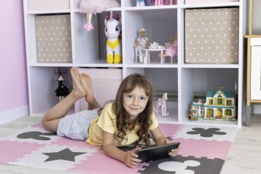 Tablet kullanan Avrupalı görünümlü küçük bir kız. Çocuk sanal oyunlar oynuyor ya da tabletinde çizgi film izliyor. Tabletli çocuk. Alet bağımlılığı sorunu..