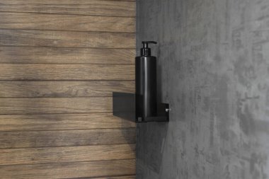 Modern bir banyo içinin duvarına asılmış minimalist siyah sabun makinesi. Temiz tasarım, beton ve ahşap dokuların kontrastı, çağdaş hijyen kavramı.