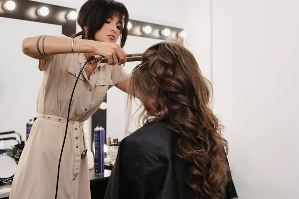 Cabeleireiro em um salão de beleza faz um penteado para uma noiva menina — Fotografia de Stock