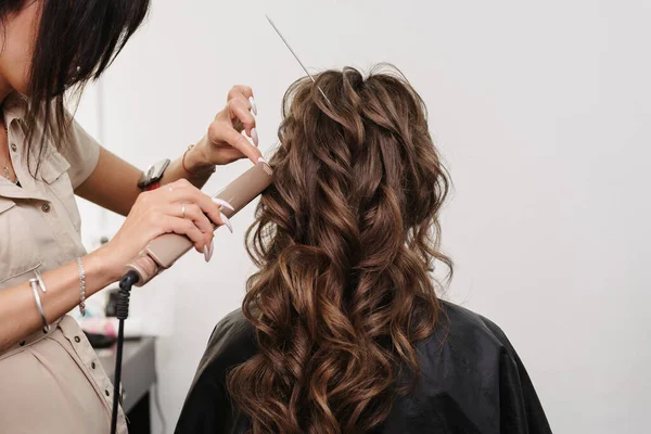 Cabeleireiro faz um penteado para uma noiva menina com longos cabelos castanhos encaracolados — Fotografia de Stock
