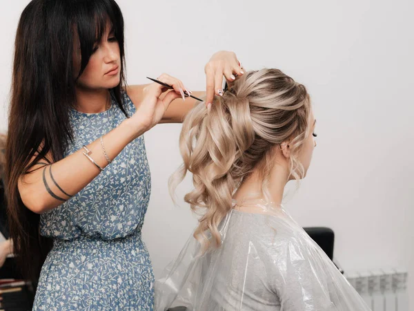 Cabeleireiro feminino faz um penteado festivo para uma loira em um salão de beleza. — Fotografia de Stock