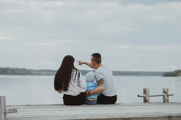 Jovem família feliz sentada no cais no verão — Fotografia de Stock