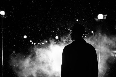 Karanlık siluet şapkalı bir adam yağmurda bir gece caddesinde bir şehirde
