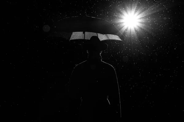 Silhouette scura di un uomo in impermeabile e cappello sotto un ombrello per strada sotto la pioggia — Foto Stock