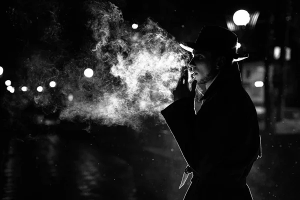 Silhouette sombre d'un homme en chapeau Fumer une cigarette sous la pluie dans une rue nocturne — Photo