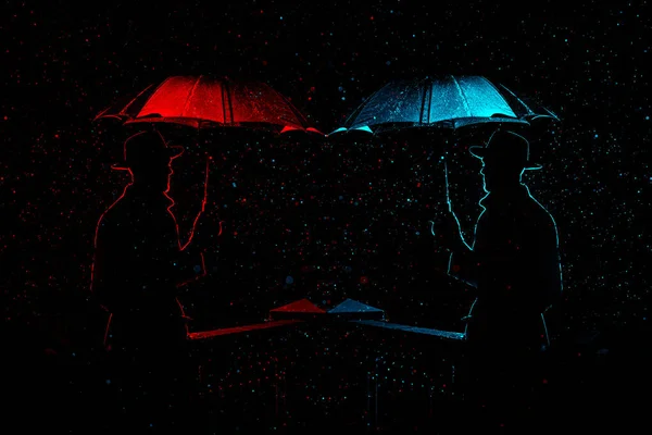 Silueta de un hombre con sombrero bajo un paraguas en la noche bajo la lluvia en la ciudad — Foto de Stock