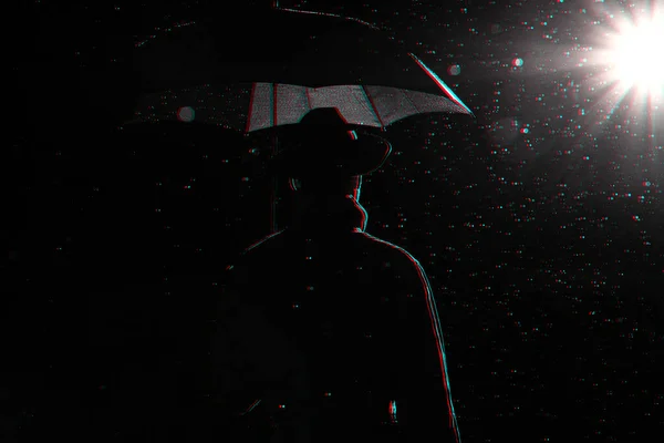 Silhouette sombre d'un homme en imperméable et chapeau sous un parapluie dans la rue sous la pluie — Photo