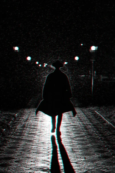 Silueta oscura de un hombre con abrigo y sombrero bajo la lluvia en una calle nocturna — Foto de Stock