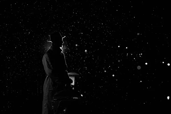 Sötét sziluett egy kalapos férfiról éjszaka az esőben a városban. — Stock Fotó