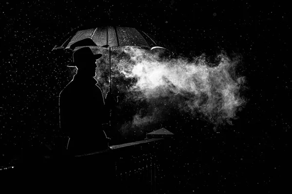 Silhouette d'un homme avec un chapeau sous un parapluie la nuit sous la pluie dans la ville — Photo