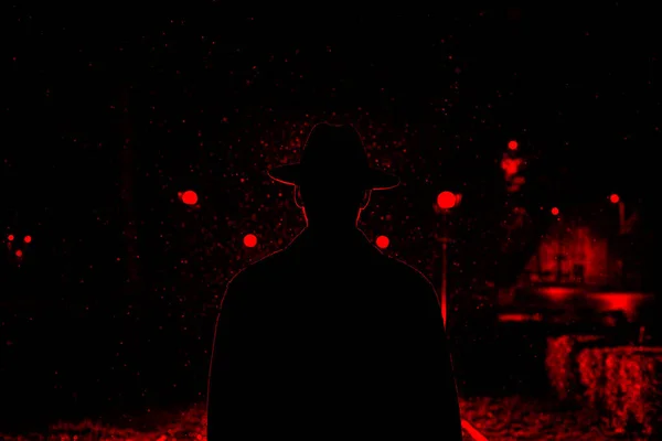 Donker silhouet van een man met een hoed in de regen op een nachtstraat — Stockfoto
