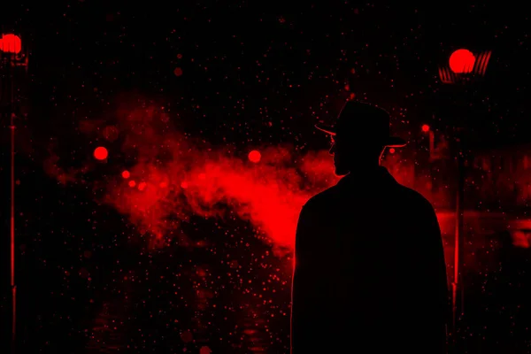 Silhueta escura de um homem com um chapéu na chuva em uma rua noturna em uma cidade — Fotografia de Stock