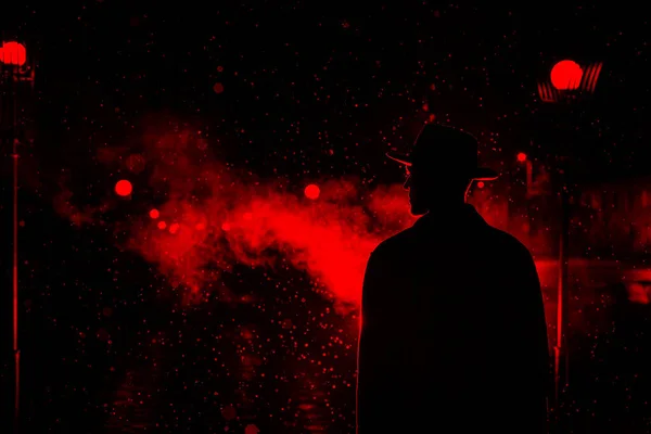 Silhouette sombre d'un homme coiffé d'un chapeau sous la pluie dans une rue nocturne d'une ville — Photo