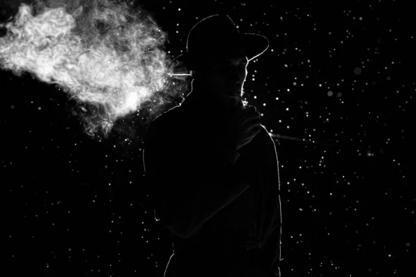 Ciemna sylwetka mężczyzny w kapeluszu palącego papierosa w deszczu — Zdjęcie stockowe