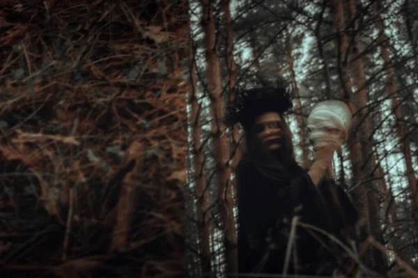 Reflexão mística turva de uma bruxa negra com um crânio nas mãos realizando um ritual satânico — Fotografia de Stock