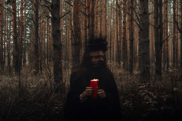 Strega in costume nero esegue incantesimi scuri con candele nella foresta — Foto Stock