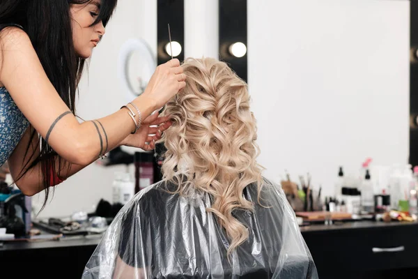 Uma menina cabeleireira coloca seus cachos em um penteado em um salão de beleza — Fotografia de Stock