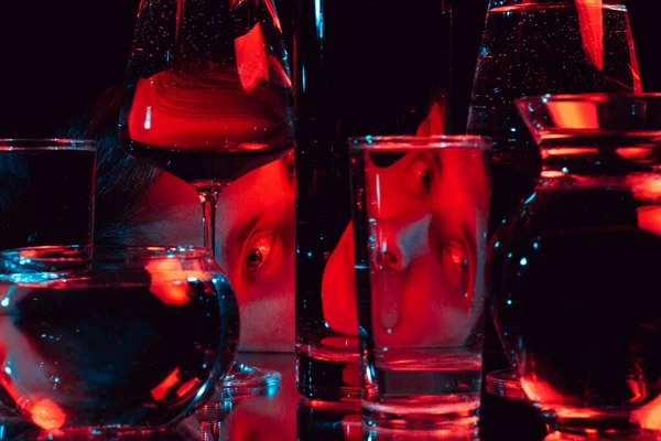 Человек смотрит сквозь стеклянные стаканы воды с отражениями и искажениями — стоковое фото