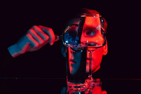 Surreal portrait of a man looking through a magnifying glass and glass glasses with water — Stock Photo, Image