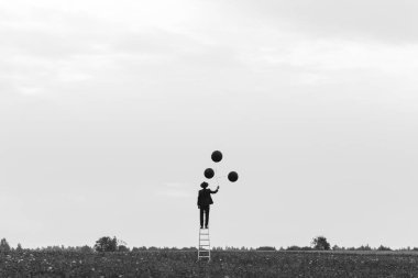 Merdivenlerde balonlarla dikilen takım elbiseli bir adamın gerçek üstü silueti.