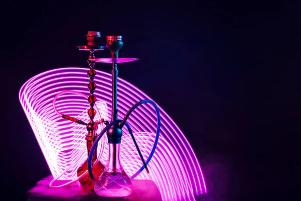 Dwie hookahs z rurami i miski i kolba wody z fioletowym oświetleniem neon — Zdjęcie stockowe
