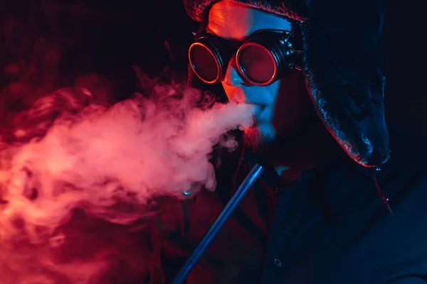 Futuristic cyberpunk portrait of a man smoking a shisha hookah and blowing a cloud of smoke — Stock Photo, Image