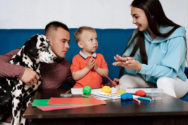 Mamma, papà, figlio e il loro cane giocano con plastilina e dipingono a casa — Foto Stock