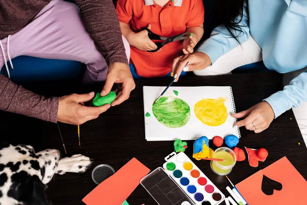 mom, dad, son and their dog play with plasticine and paint at home