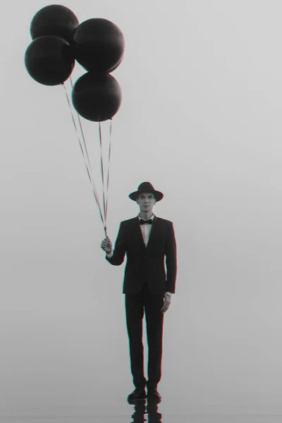 Retrato criativo surreal de um homem de terno com um chapéu com balões na mão sobre a água — Fotografia de Stock