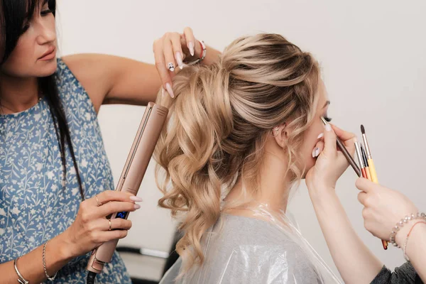Um cabeleireiro e um maquiador juntos fazem seu cabelo e maquiagem em um salão de beleza profissional — Fotografia de Stock
