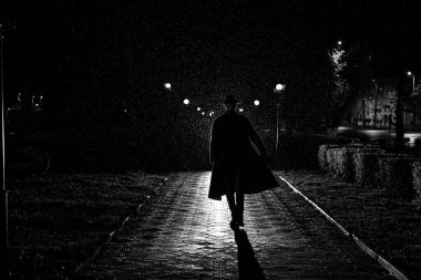 Gece sokağında yağmurda paltolu ve şapkalı bir erkek dedektifin karanlık silueti.