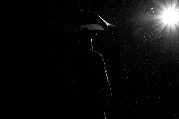 Silhouette sombre d'un homme en imperméable et chapeau sous un parapluie dans la rue sous la pluie — Photo