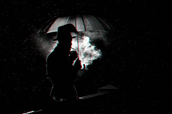 Sziluett egy kalapos férfiról esernyő alatt, aki esőben cigarettázik a városban. — Stock Fotó