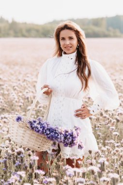Tarlada bir buket çiçekle doğada bir sepet içinde bir kız